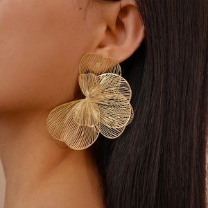Close-up of oversized gold hollow flower earrings on model highlighting metallic texture