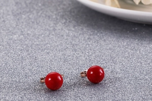 Gros plan de boucles d'oreilles boules rouges sur une surface argentée brillante et texturée