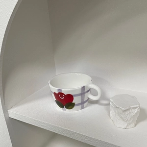 Close-up of a white ceramic mug with purple grid and red smiling cherry patterns