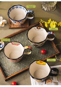 Detail of four hand-painted floral ceramic mugs with scalloped edges on a rustic tray