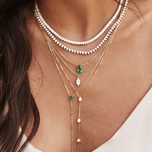 Close-up of layered gold Y-necklace with emerald green pendants and sparkling white stones