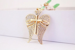 Close-up of gold-plated cross pendant with rhinestone angel wings and crown detail