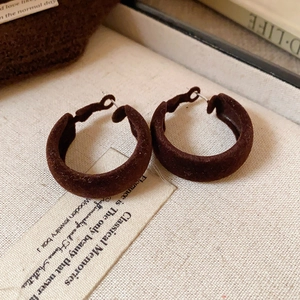 Detailed close-up of C-shaped dark brown velvet earrings on a textured fabric