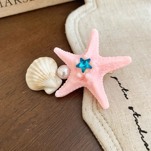 Close-up of pink starfish and shell hair clip with a sparkling blue star crystal