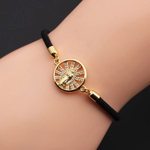 Detail eines gewebten Bohemian-Armbands mit goldenem Marienanhänger und weißem Zirkon