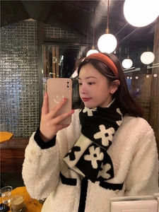 Close-up of black and white floral knit scarf worn by model in a cozy cafe setting
