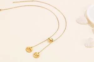 Detail of golden Y-shape necklace featuring an adjustable heart slide and engraved round charms