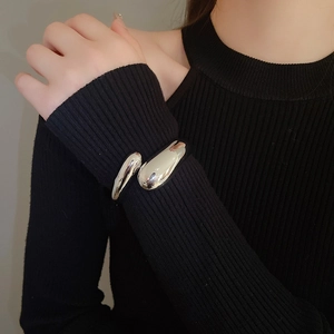 Polished silver liquid-style teardrop cuff bracelet on a model wearing black knitwear