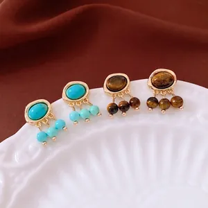 Vintage gold earrings with turquoise and tiger eye stones on an elegant ceramic plate