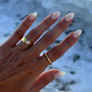Detail of 18K gold plated lava rings with a white pearl on a hand by the beach