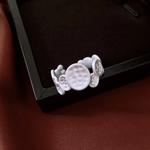 Close-up of matte white hammered texture and disc patchwork detail on the open ring