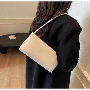 Detail view of a minimalist cream shoulder bag with slim straps worn by a model