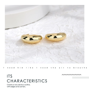 Detail of chunky gold-plated C-shaped earrings with high-polish mirror finish on white paper