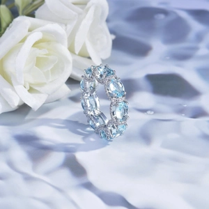 Macro detail of silver eternity ring with oval light blue gems on a reflective water surface
