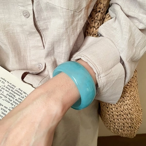 Detail of a wide translucent blue resin bangle worn with a minimalist linen outfit