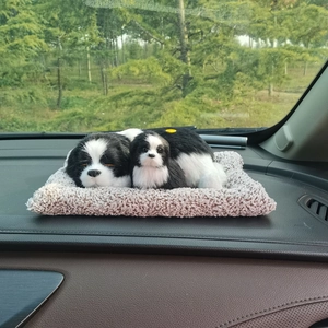 Lifelike black and white toy dogs lying on a grey plush mat on a car dashboard