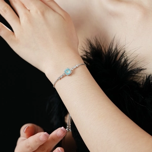Close-up of a silver adjustable bracelet with a square blue gemstone on a model's wrist