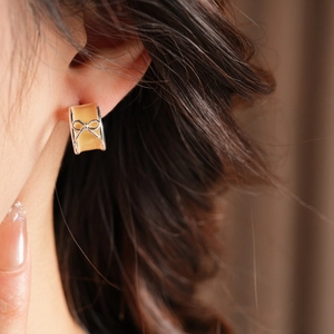 Close-up of a silver bow-knot C-shaped stud earring with amber resin on a model's ear