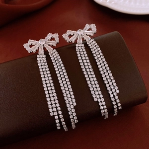 Detailed close-up of silver bow tassel earrings with sparkling zircon crystals on red velvet