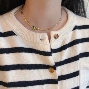 Detail of a gold snake chain necklace featuring a green enamel butterfly pendant on a model