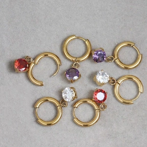 Detail of gold huggie earrings with round red, purple, and clear zircon charms