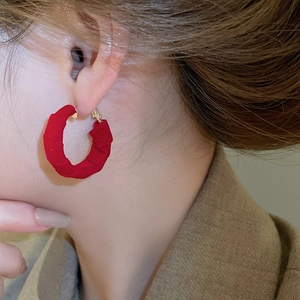 Macro shot of red fabric hoop earrings with gold clasp worn in a cozy autumn setting