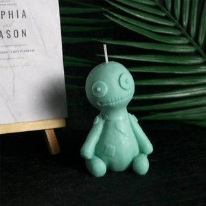 Close-up of mint green voodoo doll candle with stitch details on dark textured surface