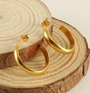 Macro detail of gold C-shaped hoop earrings with matte finish on natural wood blocks