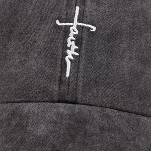 Detailed close-up of white faith cross embroidery on dark gray washed cotton baseball cap