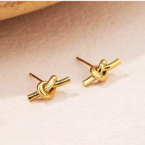 Macro detail of polished 18K gold knot stud earrings on a textured stone surface