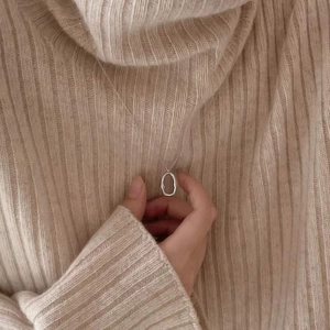 Detail of irregular silver oval pendant necklace on a beige knit sweater texture