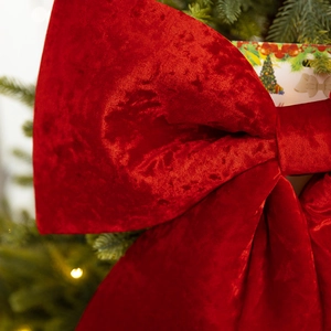 Large red velvet Christmas bow ornament hanging on a festive tree with warm bokeh lights