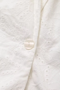 Close-up of intricate white embroidery and a pearlescent button on a suit jacket