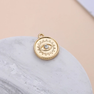 Macro shot of gold plated evil eye charm with clear crystal on white marble surface