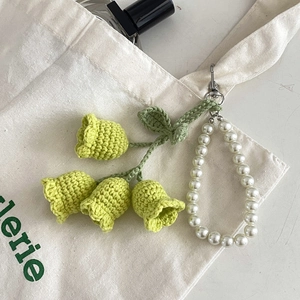 Close-up of hand-knitted lily of the valley charm with pearls on a white canvas bag