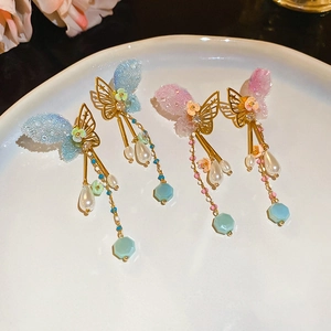Detail of butterfly tassel earring with lace wings and hanging pearl drop on white ceramic