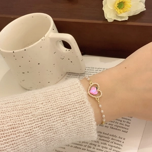 Dettaglio del bracciale con perle dorate e pietra a cuore rosa pesca sul polso di una donna