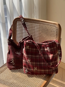 Sac à bandoulière à carreaux rouges avec nœud brodé et texture tweed sur chaise vintage