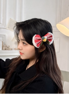 Détail d'une pince à cheveux nœud de Noël rouge avec pompons blancs sur un mannequin