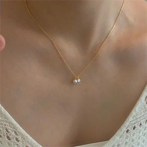 Detailed view of gold pearl necklace with zircon pendant worn on a model with lace collar