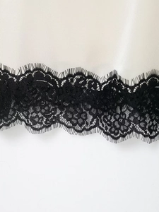 Detailed close-up of cream satin fabric with exquisite wide black lace hem finishing