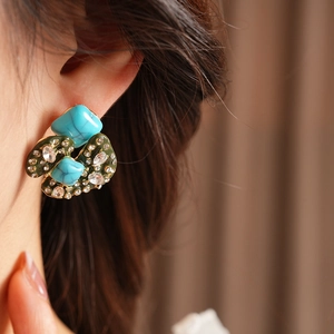 Close-up of vintage earrings with blue turquoise and green enamel on a model