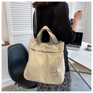 Detail view of a beige nylon tote bag with wide shoulder straps worn in an office setting