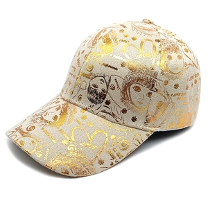 Detailed view of beige baseball cap featuring golden metallic anime graffiti print