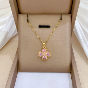 Detail of pink heart-shaped crystal clover pendant with gold chain on white satin