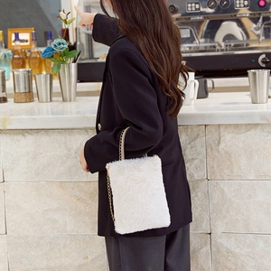 Minimalist white faux fur plush shoulder bag with gold chain worn by model in a cafe