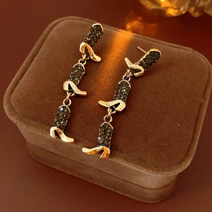 Close-up of golden triple-tier boot-shaped earrings with dark gems on brown velvet box
