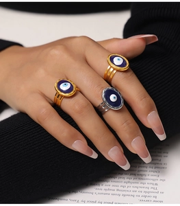 Detailed view of layered gold and silver evil eye rings on model's hand against black fabric