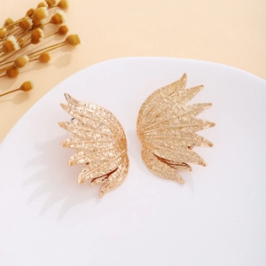 Close-up of golden wing-shaped earrings with textured finish on a white display pedestal