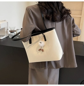Dettaglio borsa tote color crema con bordi neri e ciondolo di peluche indossata da modella